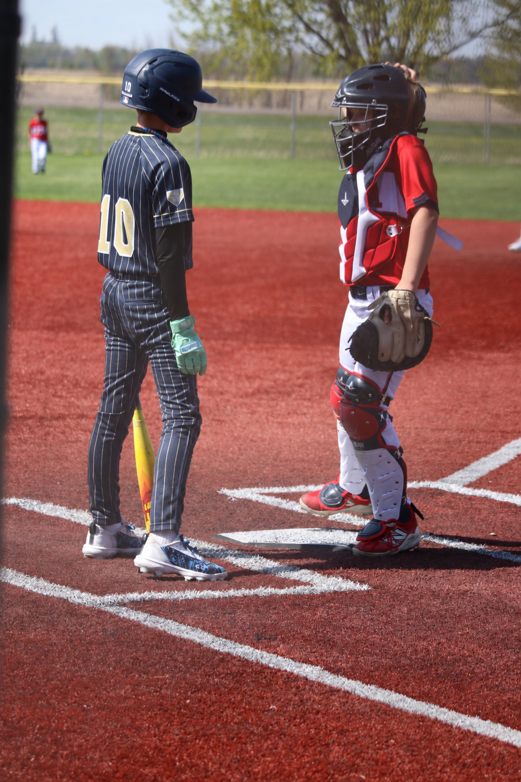Youth baseball player wearing custom TAKX cleat wraps beside the catcher