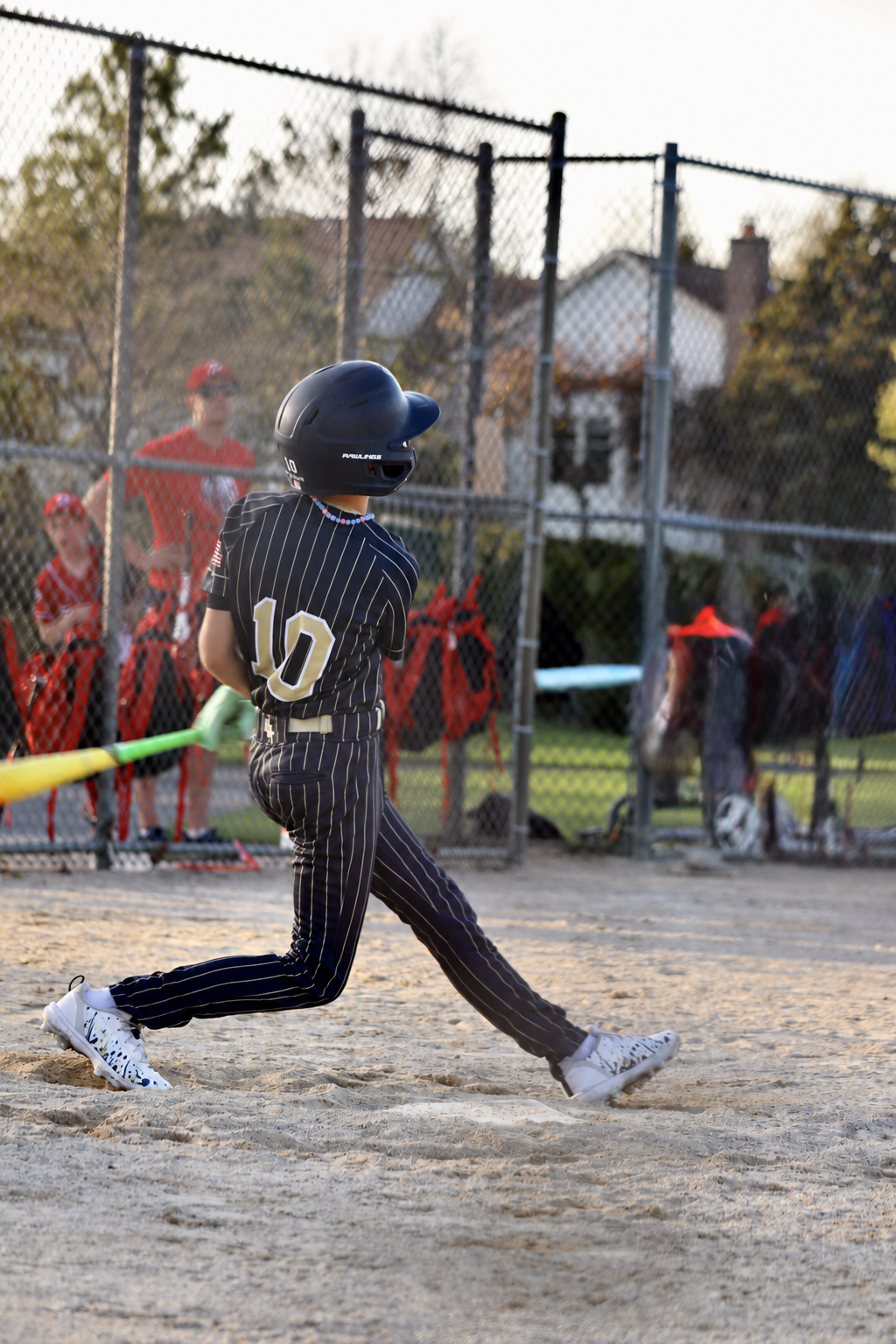 Youth baseball player swinging in custom TAKX cleat wraps